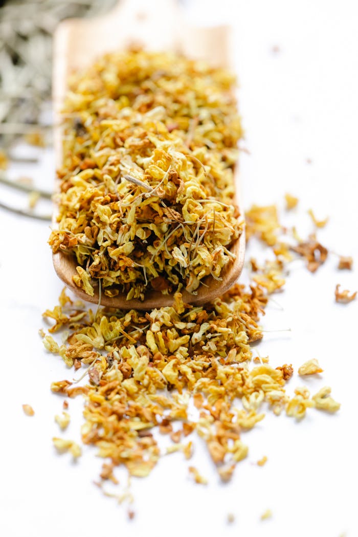 Vibrant dried yellow flower petals overflowing from a wooden scoop against a clean white background.